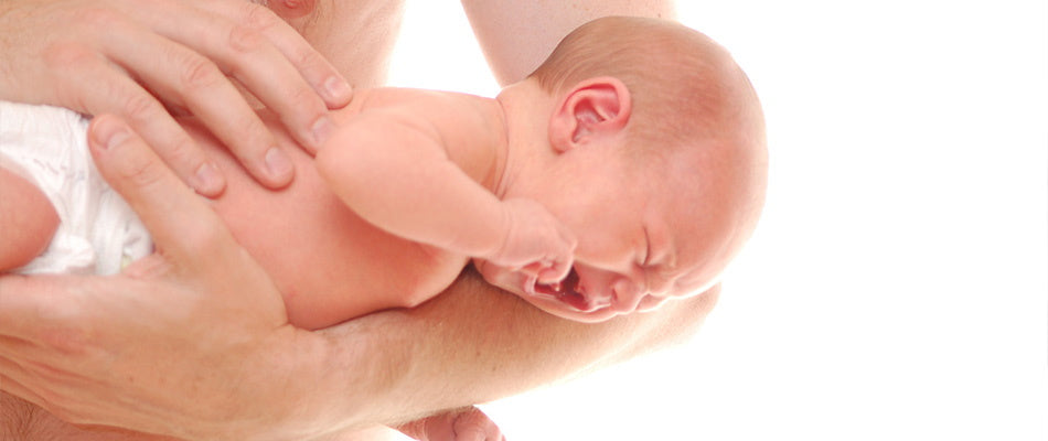 Ein weinendes Baby wird von einem Erwachsenen auf dem Arm gehalten. Das Baby trägt nur eine Windel und ist sichtlich unzufrieden.