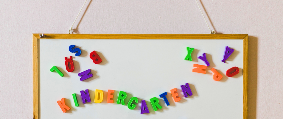 Bunte Buchstaben auf einem Whiteboard, KINDERGARTEN steht in der Mitte, andere Buchstaben verstreut.