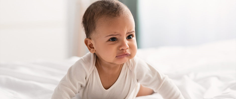 Ein Baby, das verärgert schaut und auf dem Bett sitzt.