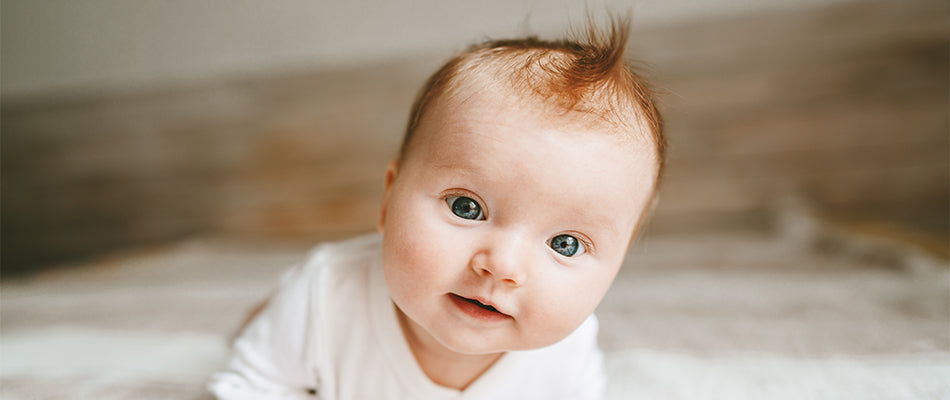 Niedliches Baby mit großen Augen und ersten Haaren, das auf dem Bauch liegt.