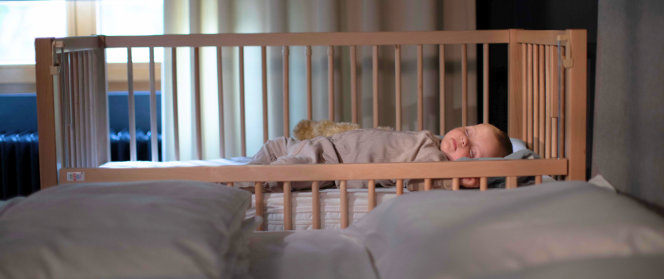 Ein Baby schläft in einem Anstellbett neben einem großen Bett.