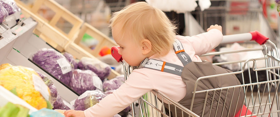 Ein Kleinkind sitzt in einem Einkaufswagen und greift nach Gemüse im Supermarkt.