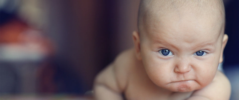 Baby mit konzentriertem, ernstem Gesichtsausdruck, zeigt Frustration  vor dem Einschlafen.