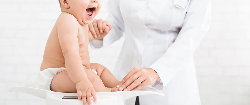 Ein Baby sitzt lachend auf einer Waage, während ein Arzt es vorsichtig hält.