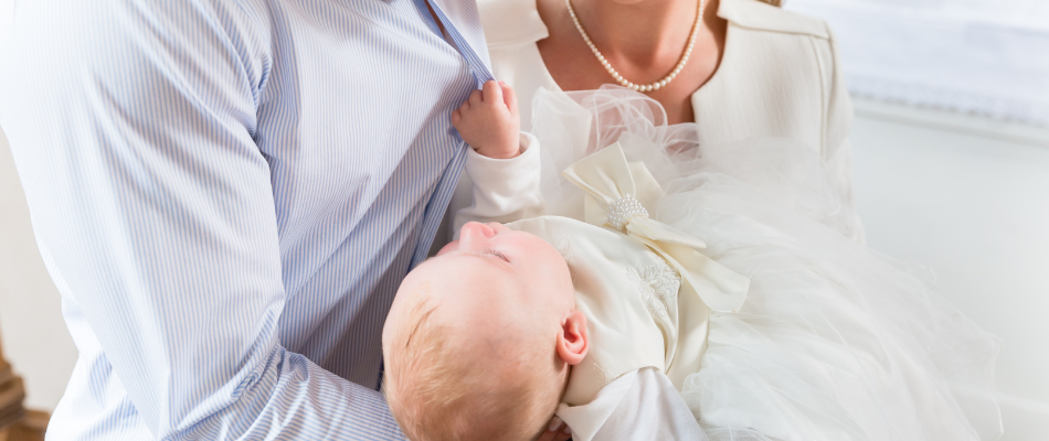 Ein Baby, das auf dem Arm eines Erwachsenen liegt und ein weißes Taufkleid trägt