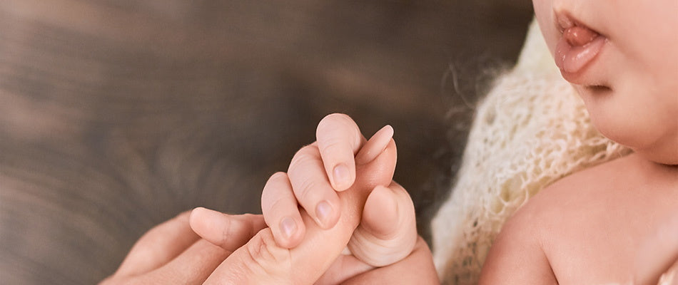 Ein Baby hält den Finger eines Erwachsenen fest, während es seine Lippen leicht geöffnet hat.