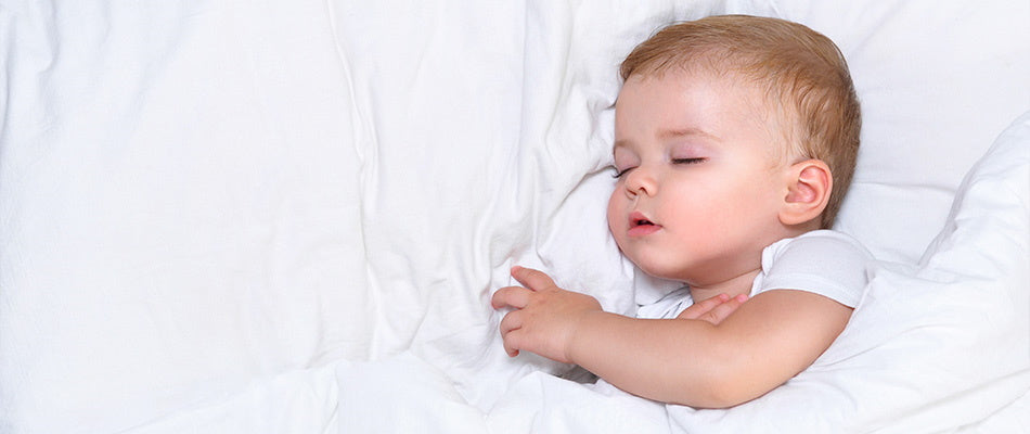 Ein Baby schläft friedlich auf dem Rücken in einem weißen Bett, umgeben von weißen Decken.